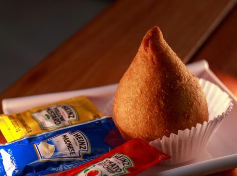 Uma coxinha em cima de uma mesa com saches de molhos ao lado