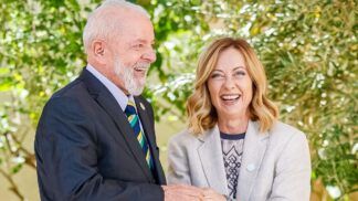 A foto mostra um encontro diplomático entre o presidente do Brasil, Luiz Inácio Lula da Silva, e a primeira-ministra da Itália, Giorgia Meloni. Ambos estão sorrindo abertamente em um momento de descontração e cumprimento.