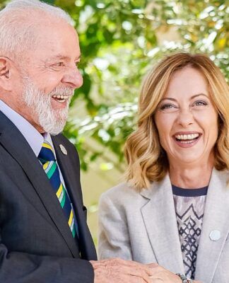 A foto mostra um encontro diplomático entre o presidente do Brasil, Luiz Inácio Lula da Silva, e a primeira-ministra da Itália, Giorgia Meloni. Ambos estão sorrindo abertamente em um momento de descontração e cumprimento.