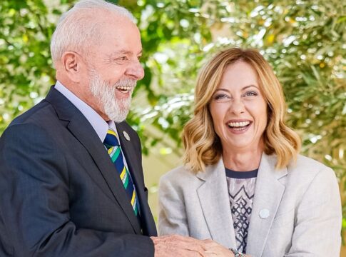 A foto mostra um encontro diplomático entre o presidente do Brasil, Luiz Inácio Lula da Silva, e a primeira-ministra da Itália, Giorgia Meloni. Ambos estão sorrindo abertamente em um momento de descontração e cumprimento.