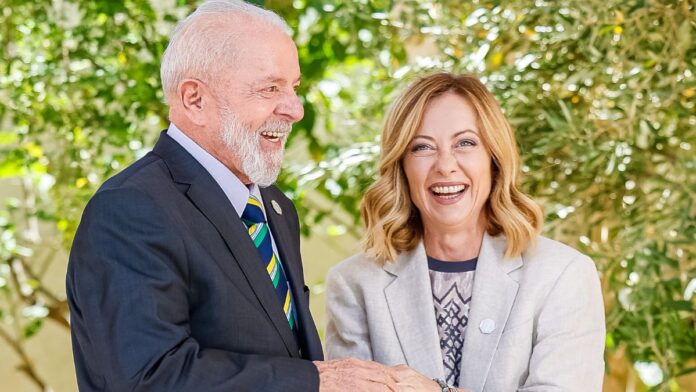 A foto mostra um encontro diplomático entre o presidente do Brasil, Luiz Inácio Lula da Silva, e a primeira-ministra da Itália, Giorgia Meloni. Ambos estão sorrindo abertamente em um momento de descontração e cumprimento.