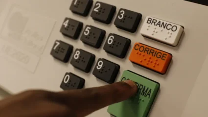 urna eletrônica de votação com foco nos botões em especial um dedo indicador apertando o botão verde