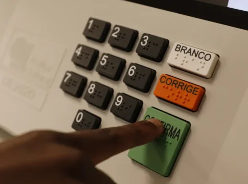 urna eletrônica de votação com foco nos botões em especial um dedo indicador apertando o botão verde