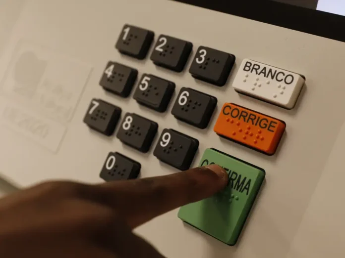 urna eletrônica de votação com foco nos botões em especial um dedo indicador apertando o botão verde