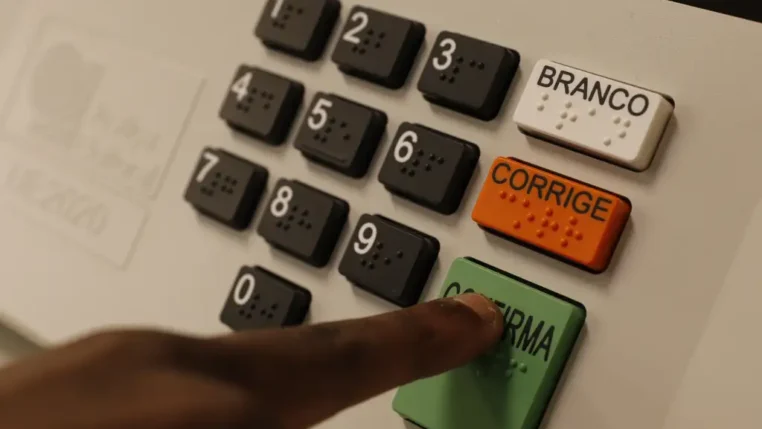 urna eletrônica de votação com foco nos botões em especial um dedo indicador apertando o botão verde
