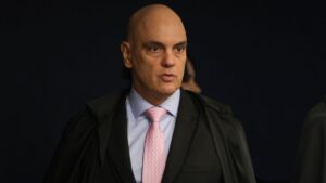 A imagem é um plano médio que foca no ministro do Supremo Tribunal Federal (STF), Alexandre de Moraes, em um ambiente interno e formal.