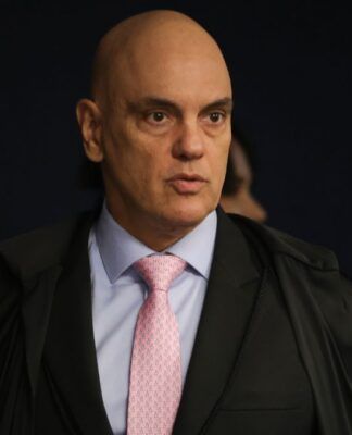 A imagem é um plano médio que foca no ministro do Supremo Tribunal Federal (STF), Alexandre de Moraes, em um ambiente interno e formal.