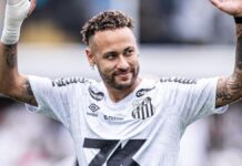A imagem é um plano médio do jogador de futebol Neymar Jr., vestindo a camisa do Santos Futebol Clube, em um momento de interação com o público ou torcida.