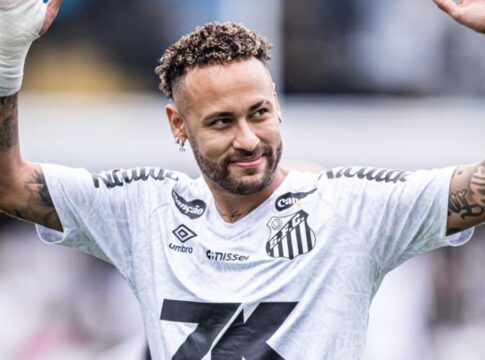 A imagem é um plano médio do jogador de futebol Neymar Jr., vestindo a camisa do Santos Futebol Clube, em um momento de interação com o público ou torcida.