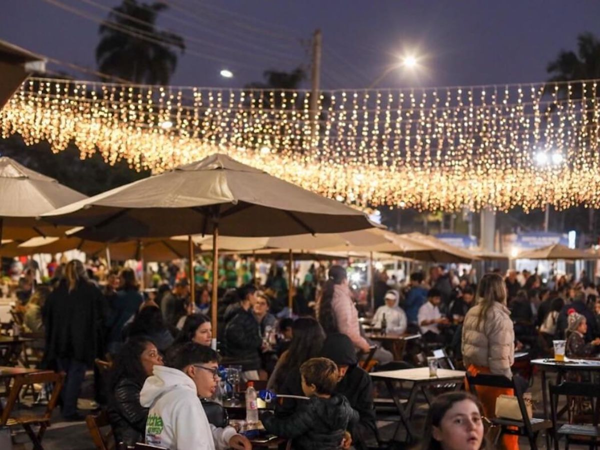 Na foto há diversas pessoas sentadas em mesas, além de pisca-piscas sob a cabeça deles.