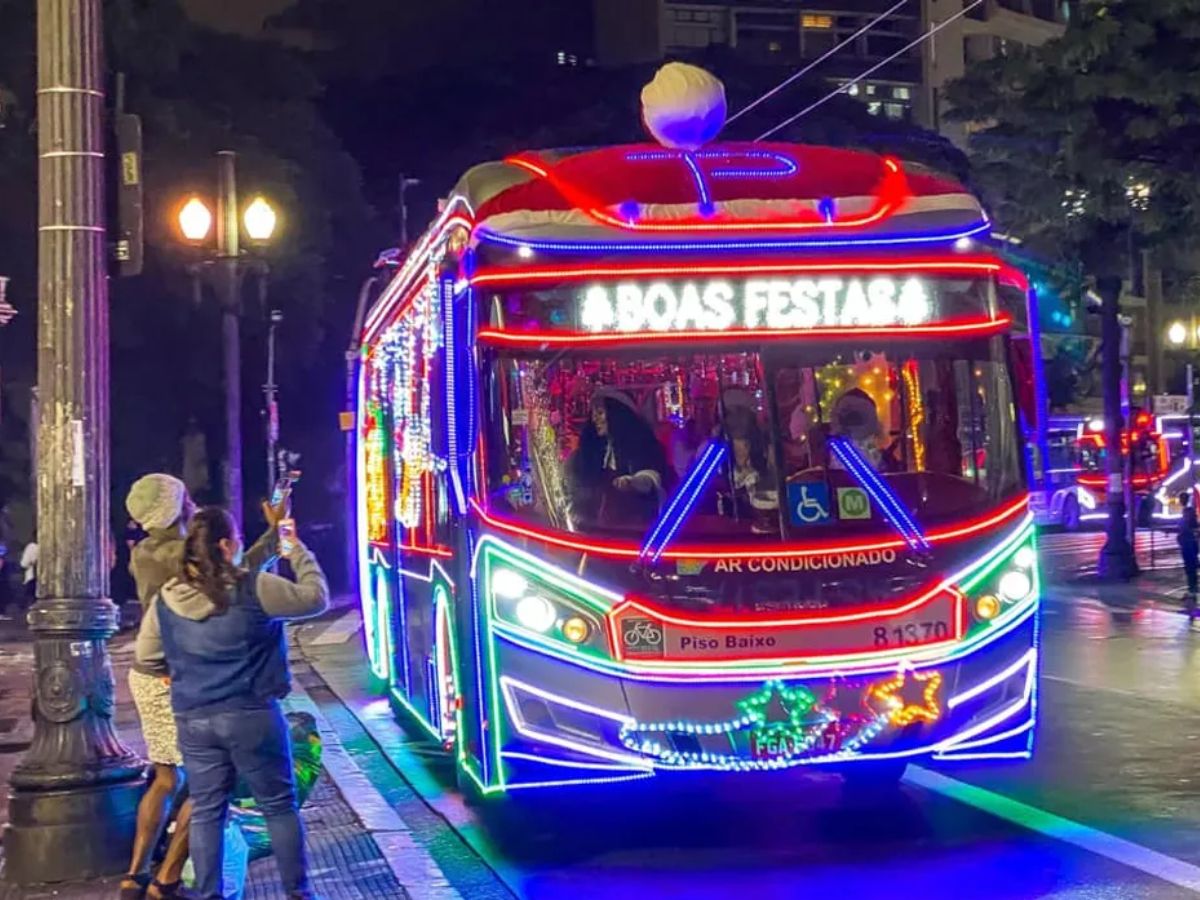 Na foto há um ônibus passando por uma rua. Ele está cheio de pisca-piscas.