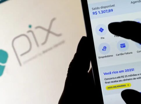 Imagem mostra a silhueta de uma mão segurando um celular e mexendo num aplicativo de banco. Atrás, aparece um fundo desfocado com a palavra 