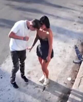 Esta é uma imagem granulada e aérea, típica de uma câmera de segurança, que captura um casal em um momento de intimidade na rua, próximo à calçada. O casal é composto por Douglas da Silva e Tainara Souza. Ele a atropelou e arrastou na Marginal Tietê.