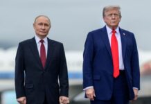 A imagem é um plano médio que captura os presidentes Vladimir Putin e Donald Trump lado a lado, em pé, em um ambiente externo que se assemelha a uma pista de aeroporto ou área externa de recepção, sob um céu nublado.