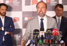 Esta é uma fotografia tirada em um ambiente interno, durante o que parece ser uma coletiva de imprensa ou anúncio oficial, focada em três figuras políticas masculinas em primeiro plano, com microfones e um painel de fundo. O primeiro, falando para microfones, é Alexandre Silveira. Atrás dele, aparecem Ricardo Nunes e Tarcísio de Freitas.