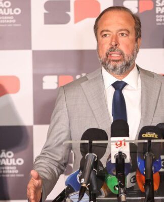 Esta é uma fotografia tirada em um ambiente interno, durante o que parece ser uma coletiva de imprensa ou anúncio oficial, focada em três figuras políticas masculinas em primeiro plano, com microfones e um painel de fundo. O primeiro, falando para microfones, é Alexandre Silveira. Atrás dele, aparecem Ricardo Nunes e Tarcísio de Freitas.