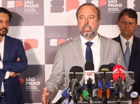 Esta é uma fotografia tirada em um ambiente interno, durante o que parece ser uma coletiva de imprensa ou anúncio oficial, focada em três figuras políticas masculinas em primeiro plano, com microfones e um painel de fundo. O primeiro, falando para microfones, é Alexandre Silveira. Atrás dele, aparecem Ricardo Nunes e Tarcísio de Freitas.