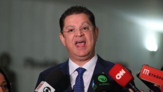 A foto apresenta um primeiro plano (close-up) do deputado Sóstenes Cavalcante durante uma entrevista ou declaração à imprensa em um ambiente interno. Ele está centralizado na imagem, voltado para a frente.