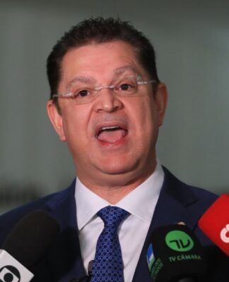 A foto apresenta um primeiro plano (close-up) do deputado Sóstenes Cavalcante durante uma entrevista ou declaração à imprensa em um ambiente interno. Ele está centralizado na imagem, voltado para a frente.