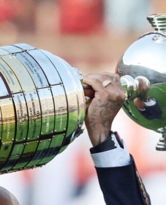A foto mostra um registro em close-up e em ângulo lateral da Taça Libertadores da América sendo erguida por um jogador. O troféu está na horizontal, ocupando grande parte do quadro.