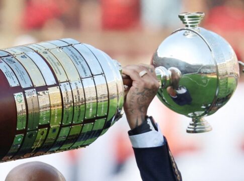 A foto mostra um registro em close-up e em ângulo lateral da Taça Libertadores da América sendo erguida por um jogador. O troféu está na horizontal, ocupando grande parte do quadro.