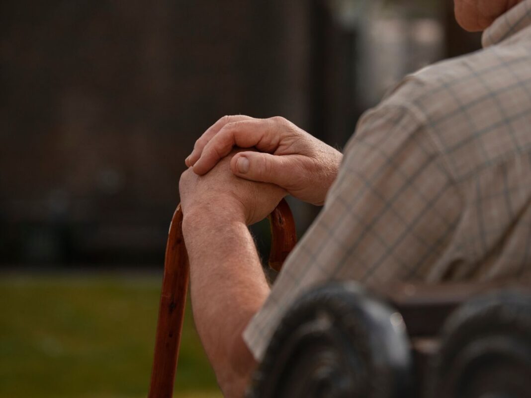 Imagem ilustrativa mostra idoso, sentado em cadeira e usando bengala