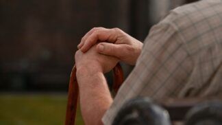 Imagem ilustrativa mostra idoso, sentado em cadeira e usando bengala