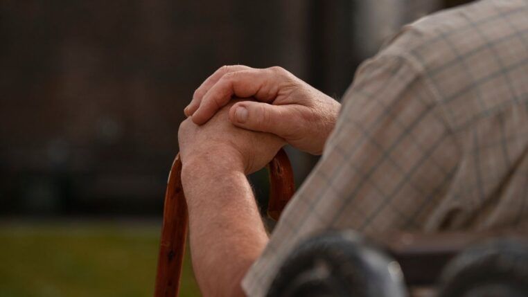 Imagem ilustrativa mostra idoso, sentado em cadeira e usando bengala