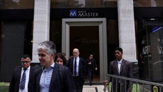 Um segurança segura uma grade enquanto pessoas deixam o Banco Master após a prisão do acionista controlador da instituição, Daniel Vorcaro