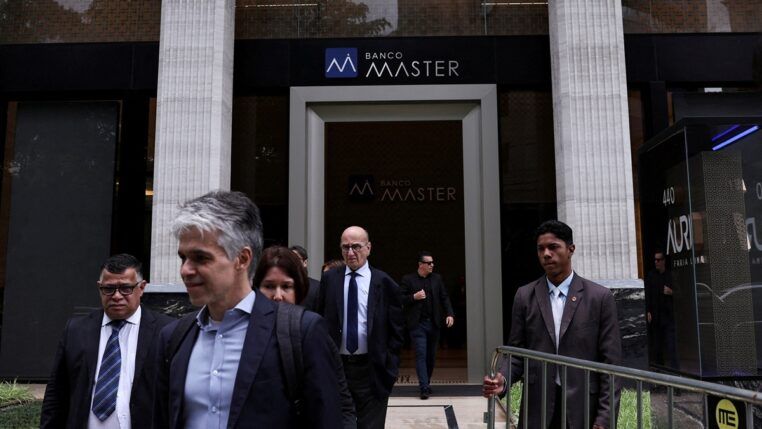 Um segurança segura uma grade enquanto pessoas deixam o Banco Master após a prisão do acionista controlador da instituição, Daniel Vorcaro