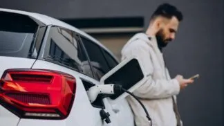 Homem carregando carro elétrico perto da casa