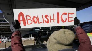 Pessoa segura um cartaz escrito: "Abolish ICE"