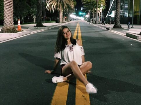 Foto de Maisa há dez ano sentada em uma rua com palmeiras na calçada