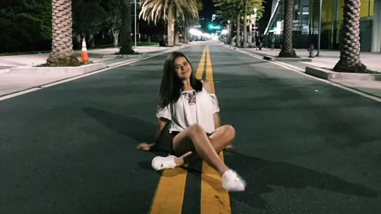 Foto de Maisa há dez ano sentada em uma rua com palmeiras na calçada