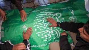 Homens com as mãos sobre uma bandeira do Hamas