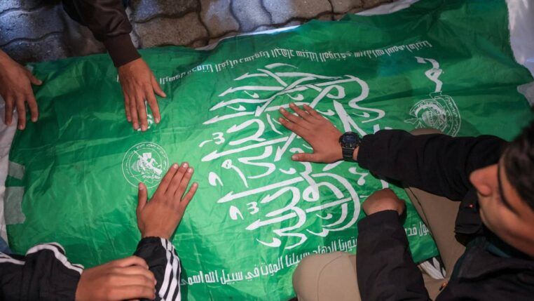 Homens com as mãos sobre uma bandeira do Hamas