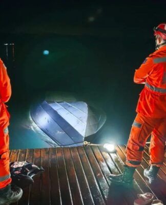 Dois profissionais do Corpo de Bombeiros observam lancha afundada