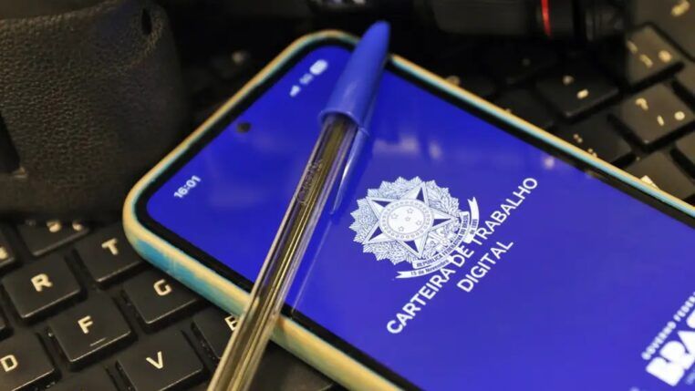 Imagem da carteira de trabalho virtual, na tela de um celular, e uma caneta