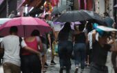 Pessoas caminhando na rua sob chuva e com guarda-chuva