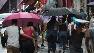 Pessoas caminhando na rua sob chuva e com guarda-chuva