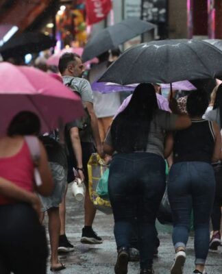 Pessoas caminhando na rua sob chuva e com guarda-chuva