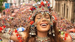 Anitta de olhos fechados e fantasiada de orixá em cima do bloco, com multidão atrás