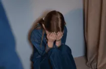 Criança sentada no chão cobrindo o rosto