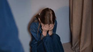 Criança sentada no chão cobrindo o rosto