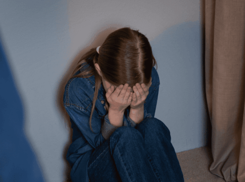 Criança sentada no chão cobrindo o rosto