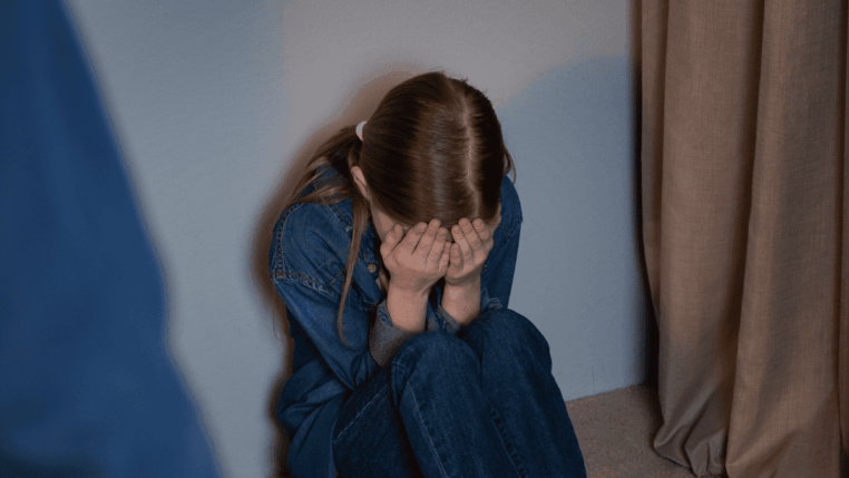 Criança sentada no chão cobrindo o rosto