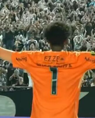 Um goleiro de costas, vestindo uma camisa laranja vibrante com o número 1 e o patrocínio 