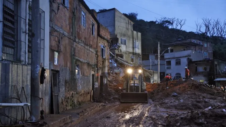 Soldados do Corpo de Bombeiros e voluntários fazem busca e resgate de pessoas em escombros de casas soterradas por lama após fortes chuvas