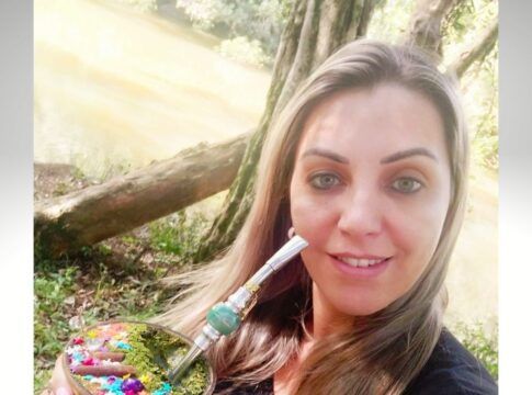 Roseli Vanda Pires Albuquerque tomando chimarrão em espaço público aberto, aparentemente um parque, perto de uma árvore