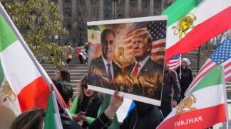 Um manifestante, diante de bandeiras pré-Revolução Iraniana com o símbolo “Leão e Sol”, exibe um cartaz com imagens do presidente dos EUA, Donald Trump, e de Reza Pahlavi, filho exilado do último xá do Irã, durante protesto em solidariedade ao povo iraniano em Washington, D.C., nos Estados Unidos
